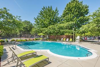 A swimming pool with yellow chairs and trees and a blue sky